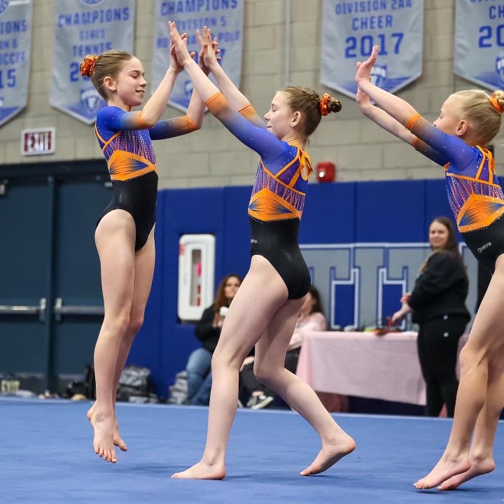 Three gymnasts jumping together on the floor