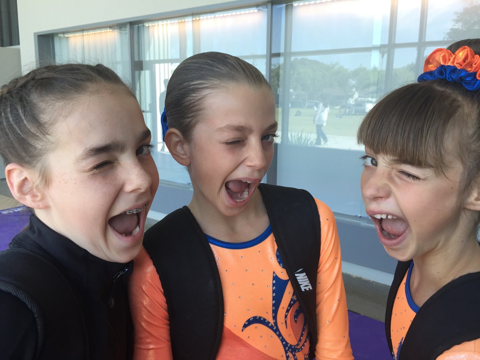 Three teammates making playful faces together in their orange leotards