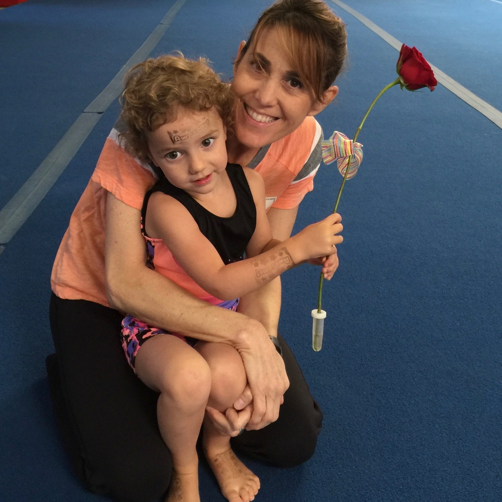 Adult hugging a young gymnast holding a rose on the gym floor