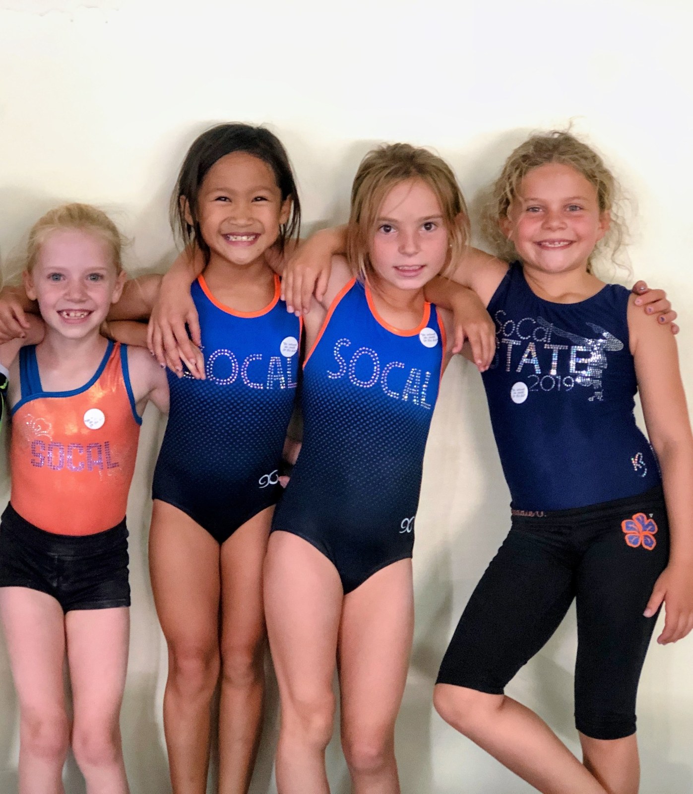 Four young SoCal teammates smiling together in blue and orange gym attire