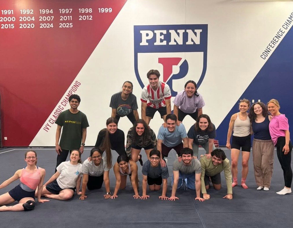 Penn gymnastics club members posing beneath the university emblem